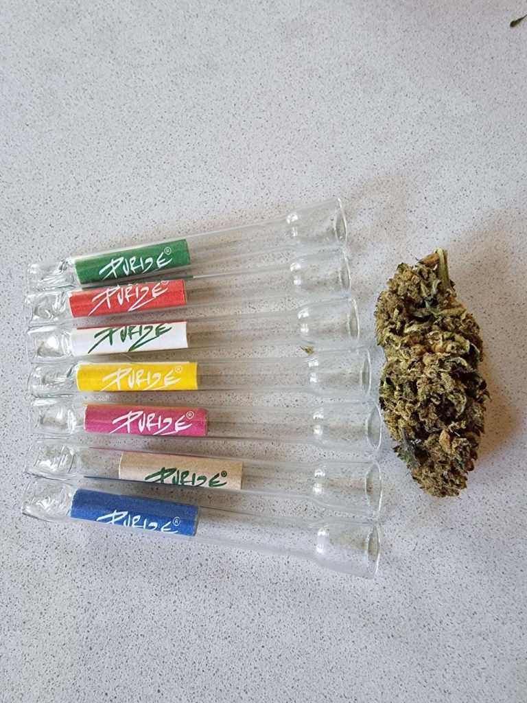 Szklane lufki z filtrami Purize w różnych kolorach, korpusy przezroczyste, obok leży kwiatostan konopi