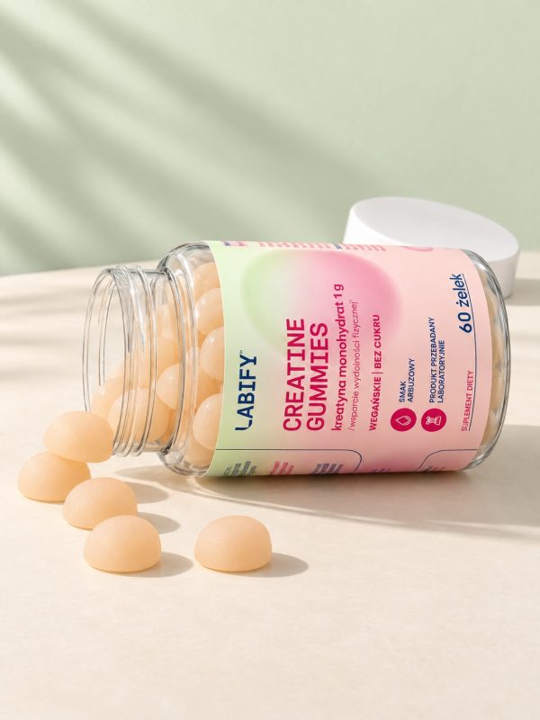 Otwarty słoik Creatine Gummies leży na boku, przed nim wysypane beżowe żelki z kreatyną
